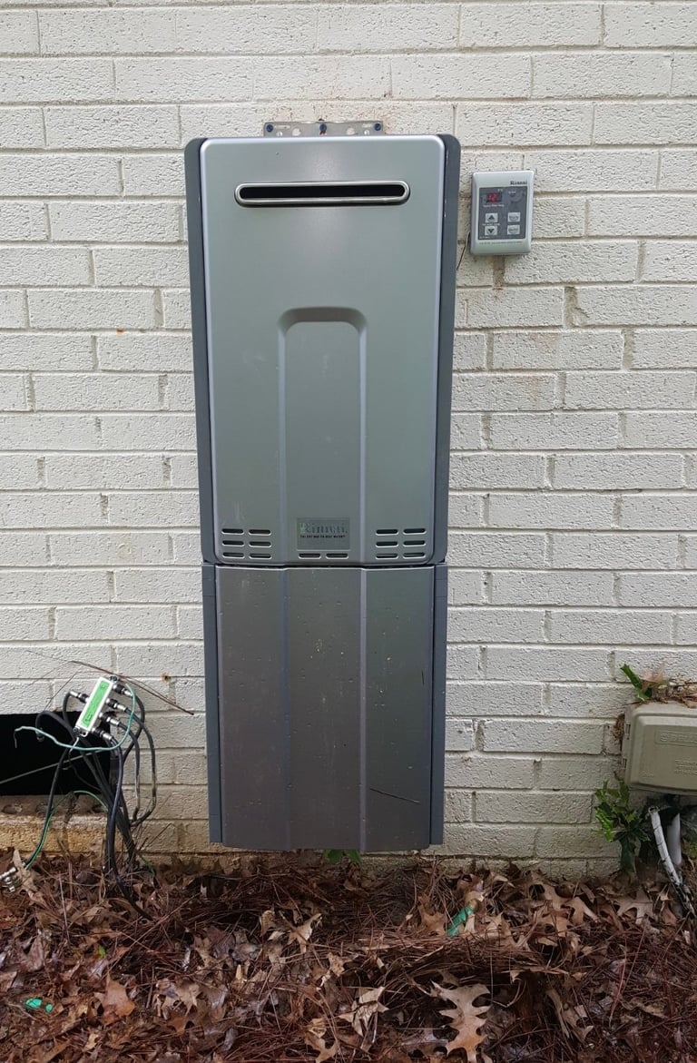 Tankless water heater mounted on brick wall with digital control panel and ground-level placement