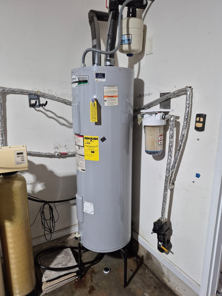 Tall gray electric water heater with black pipes and yellow warning labels mounted on basement wall