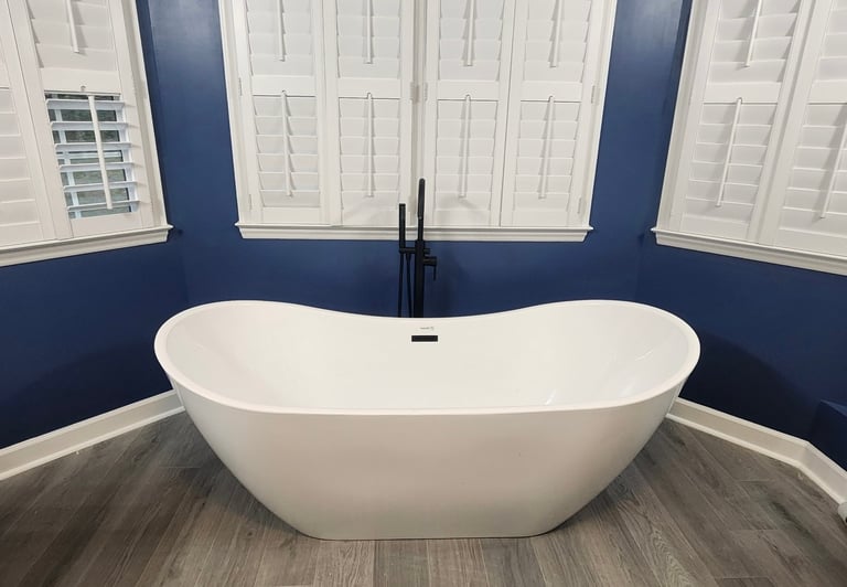 Modern white oval freestanding bathtub with black faucet in a luxury bathroom with navy blue walls and wood-look flooring