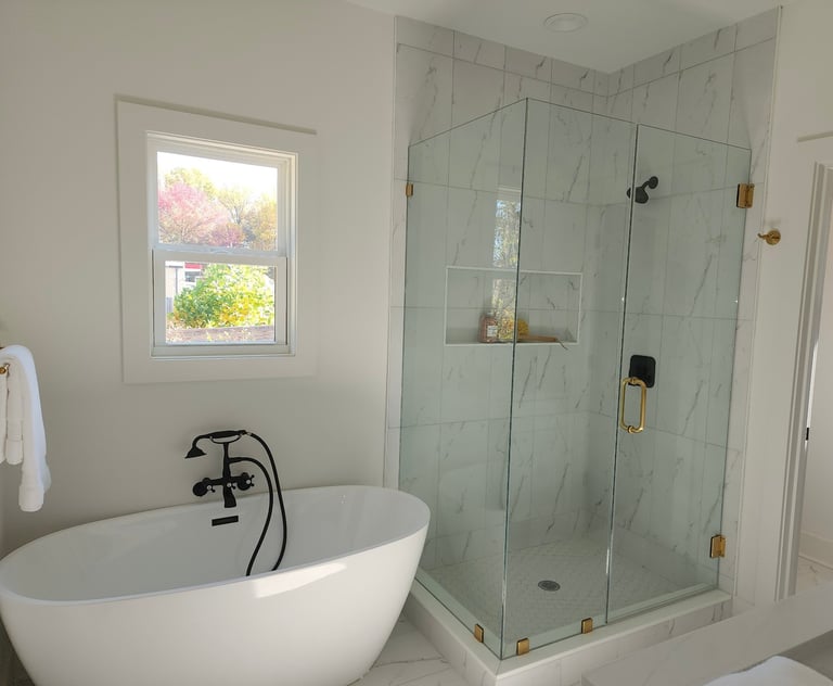 Modern bathroom with white freestanding soaking tub, glass shower enclosure, and window overlooking trees